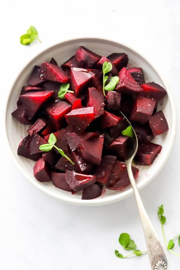 A bowl containing cooked, chopped beets with a serving spoon.