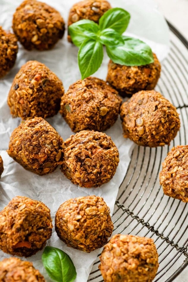 Vegan lentil meatballs with fresh basil on a cooling rack lined with parchment paper.