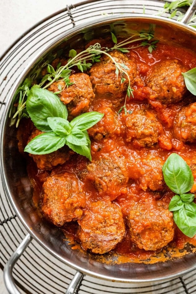 Vegan lentil meatballs, fresh basil and fresh time in a pot with sauce.