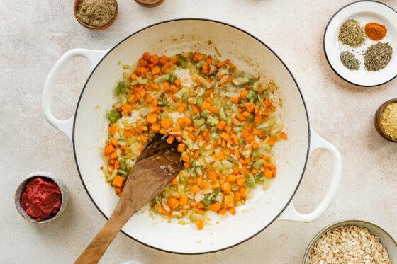 Carrots, onions, celery and garlic cooking in the bottom of a pot with a wooden spoon.