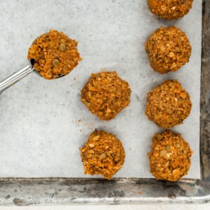 A 1 1/2 tablespoon scoop filled with lentil mixture next to several lentil meatballs on a parchment lined baking sheet.