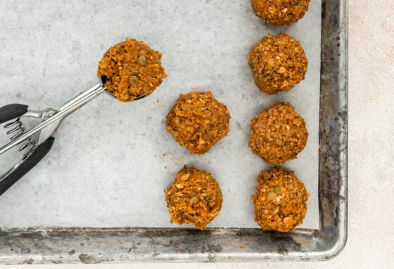 A 1 1/2 tablespoon scoop filled with lentil mixture next to several lentil meatballs on a parchment lined baking sheet.