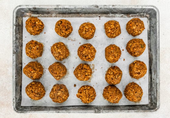 Twenty baked lentil meatballs arranged on a parchment lined baking sheet.