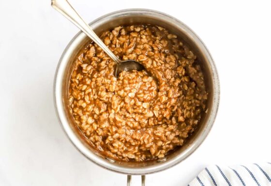 Cooked oatmeal in a pot with a metal spoon.