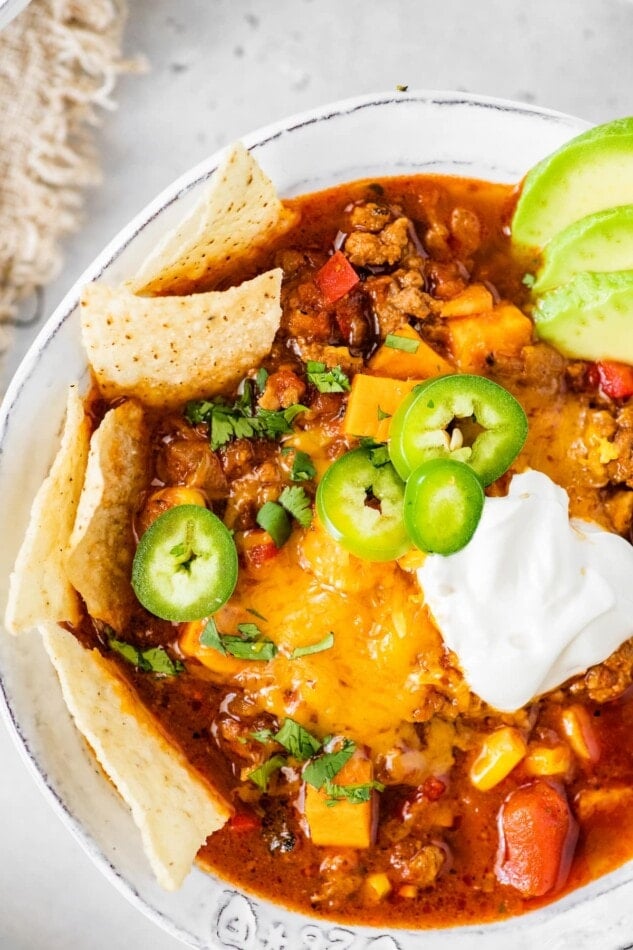 A bowl of no bean chili topped with cheese, jalapeños, avocado, sour cream and chips.