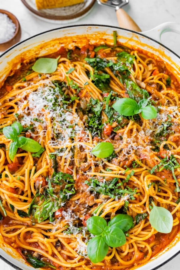 Close up of one pot pasta in a pot topped with fresh basil and grated parmesan.