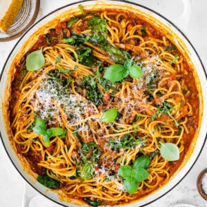 A pot containing one pot pasta topped with fresh basil and grated parmesan.