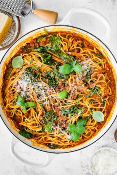 A pot containing one pot pasta topped with fresh basil and grated parmesan.