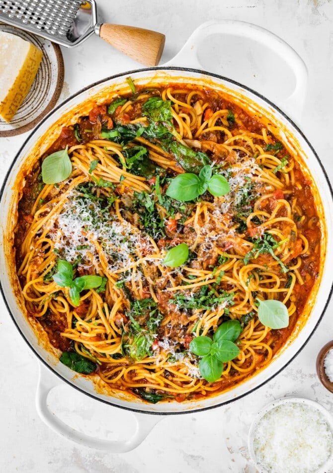 A pot containing one pot pasta topped with fresh basil and grated parmesan.