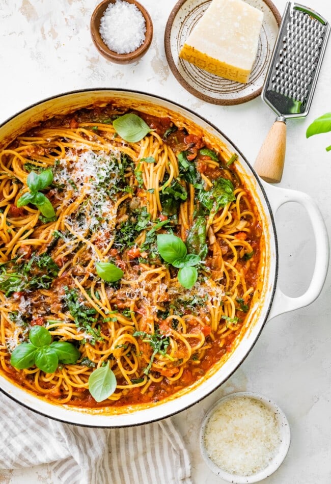 A pot containing one pot pasta topped with fresh basil and grated parmesan.