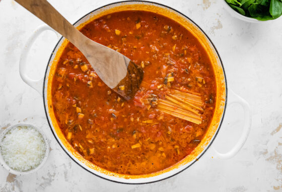 Dry spaghetti noodles being pushed into the sauce in a pot.