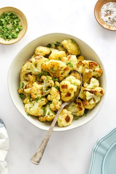 A bowl of roasted cauliflower. A serving spoon rests in the bowl.