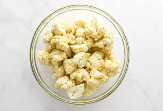 Cauliflower florets tossed in spices in a glass mixing bowl.