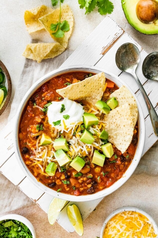 A bowl of taco soup topped with avocado chunks, shredded cheese and sour cream with tortilla chips.