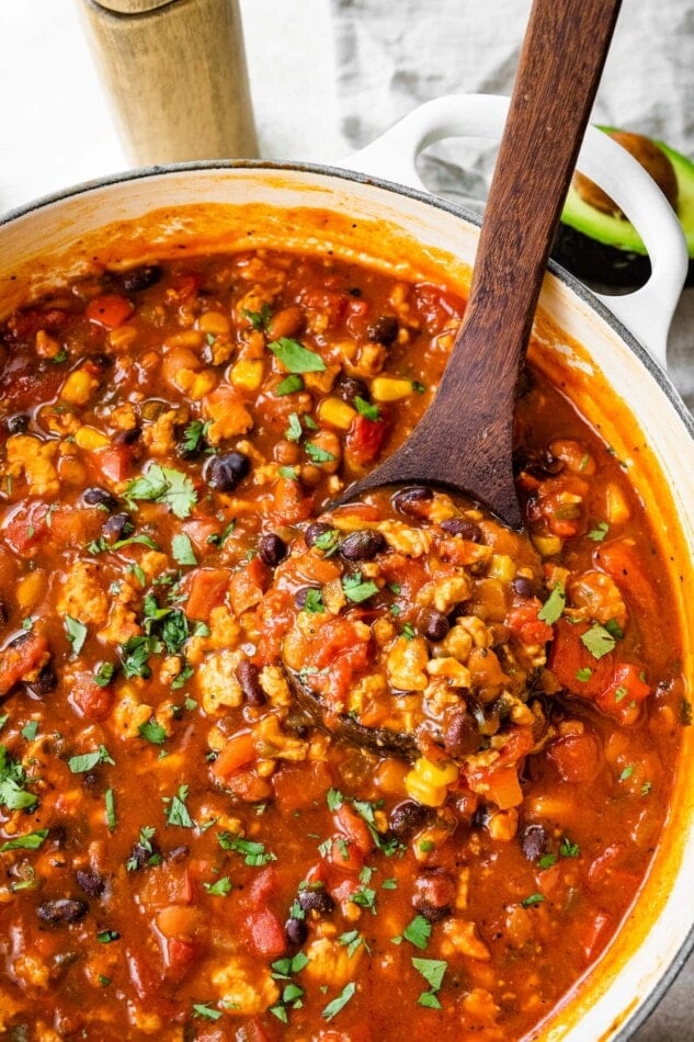 A wooden spoon ladling out a serving of taco soup from a pot.