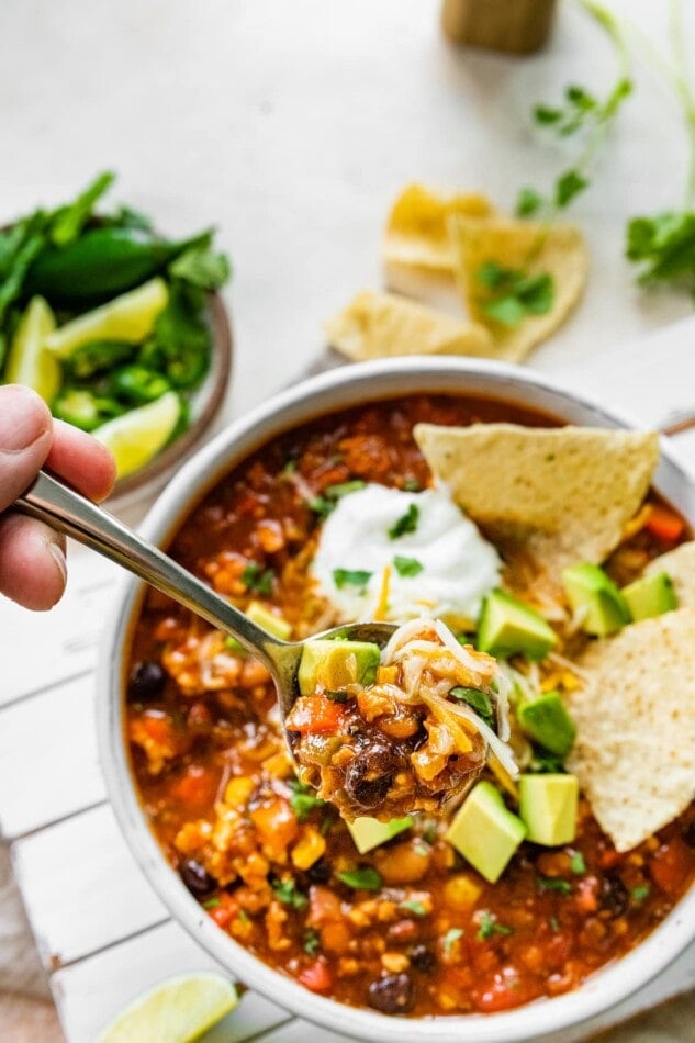 A bowl with a bite of taco soup hovering over a bowl of soup.