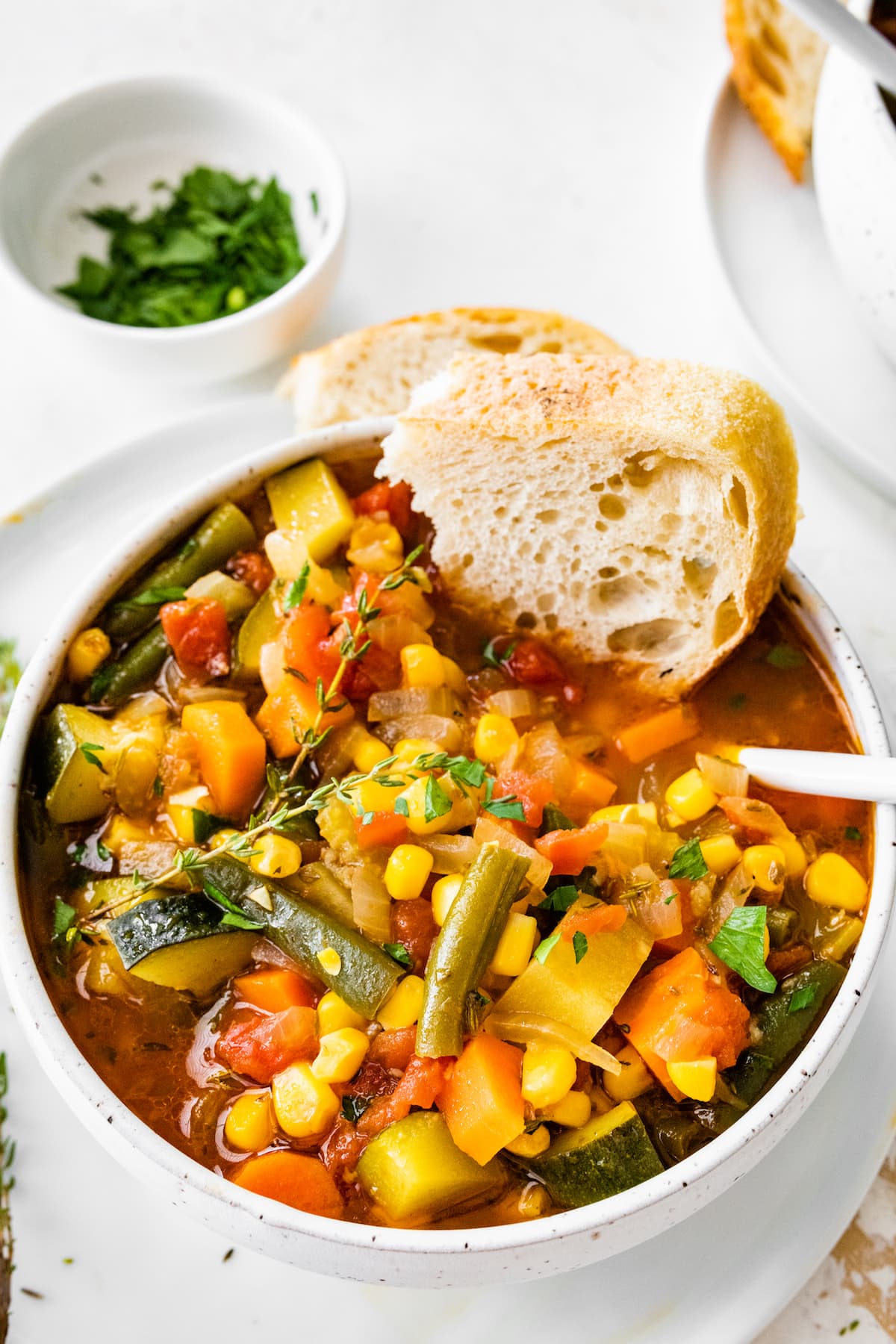 A bowl of vegetable soup with a chunk of bread dipped in the soup.