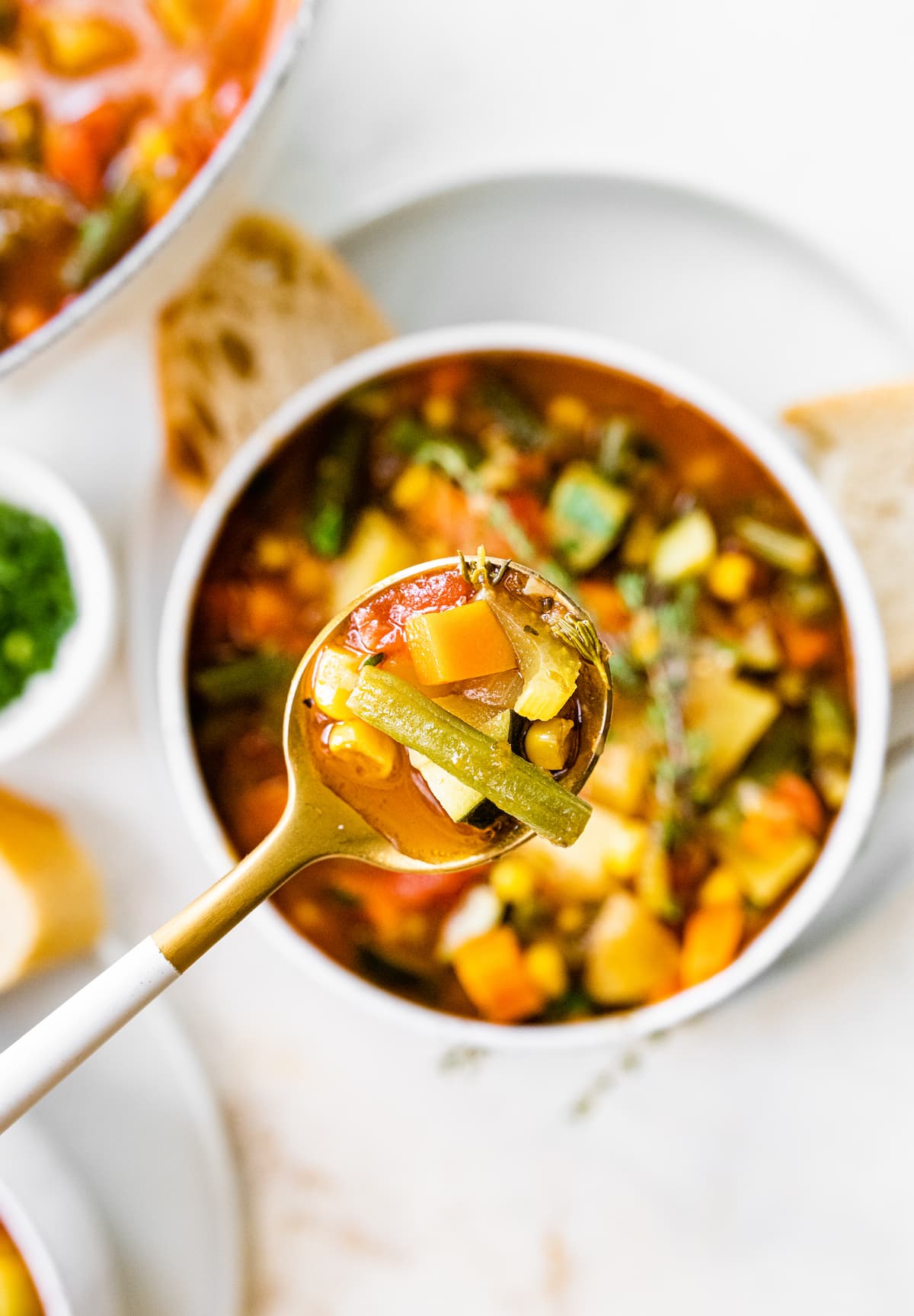 A spoonful of vegetable soup over a bowl.