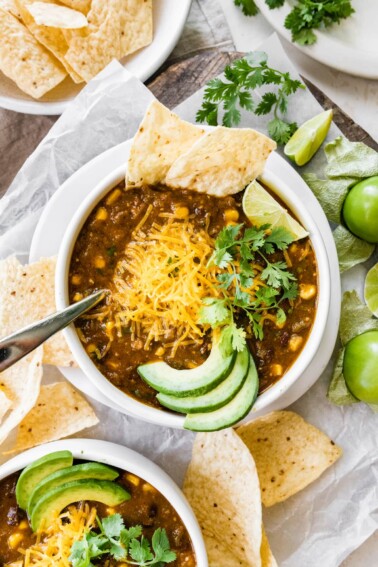 A bowl of vegetarian chili verde served with avocado, lime, cheese, cilantro and a tortilla.