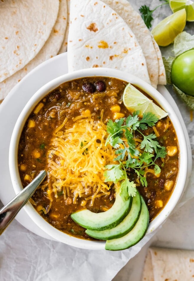 A bowl of vegetarian green chili served with shredded cheese, avocado, lime and cilantro.