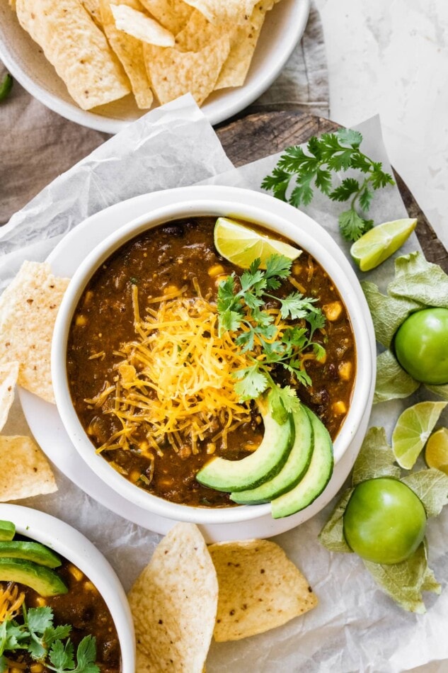 A bowl of vegetarian green chili served with shredded cheese, avocado, lime and cilantro.