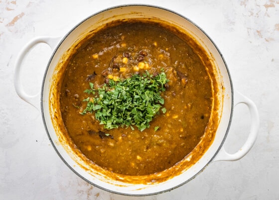 Chopped cilantro added to chili verde in pot.