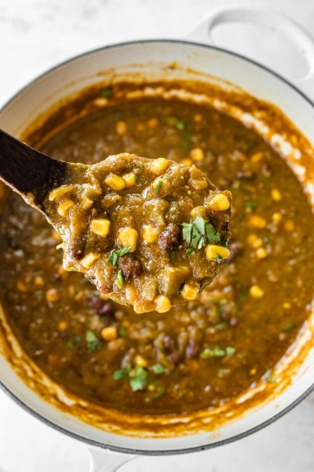 A spoonful of green chili (chili verde) over a pot.