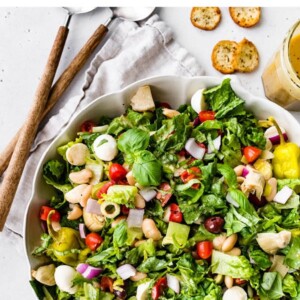 Antipasto salad in a large serving bowl. Crackers and serving spoons are next to the bowl.