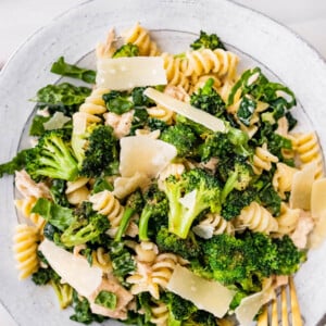 Tuna, broccoli and kale caesar pasta salad on a plate topped with shaved parmesan.