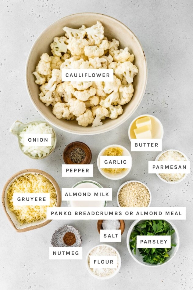 Ingredients measured out to make Cauliflower Gratin: cauliflower, onion, butter, pepper, garlic, parmesan, gruyere, almond milk, panko or almond meal, nutmeg, salt, flour and parsley.