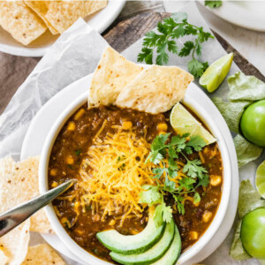 A bowl of vegetarian chili verde served with avocado, lime, cheese, cilantro and a tortilla.