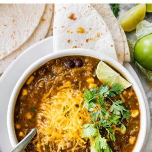 A bowl of vegetarian chili verde served with avocado, lime, cheese, cilantro and a tortilla.