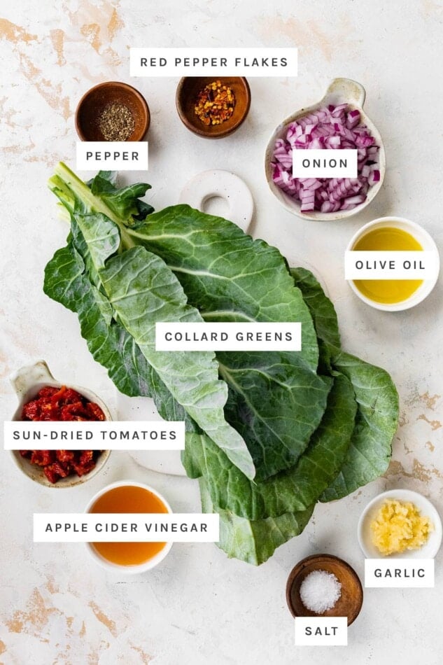 Ingredients measured out to make Raw Collard Greens Salad: red pepper flakes, pepper, onion, olive oil, collard greens, sun-dried tomatoes, apple cider vinegar, salt and garlic.