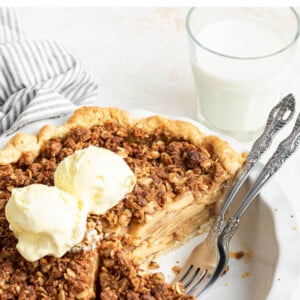 A dutch apple pie topped with ice cream in a pie plate with two forks.