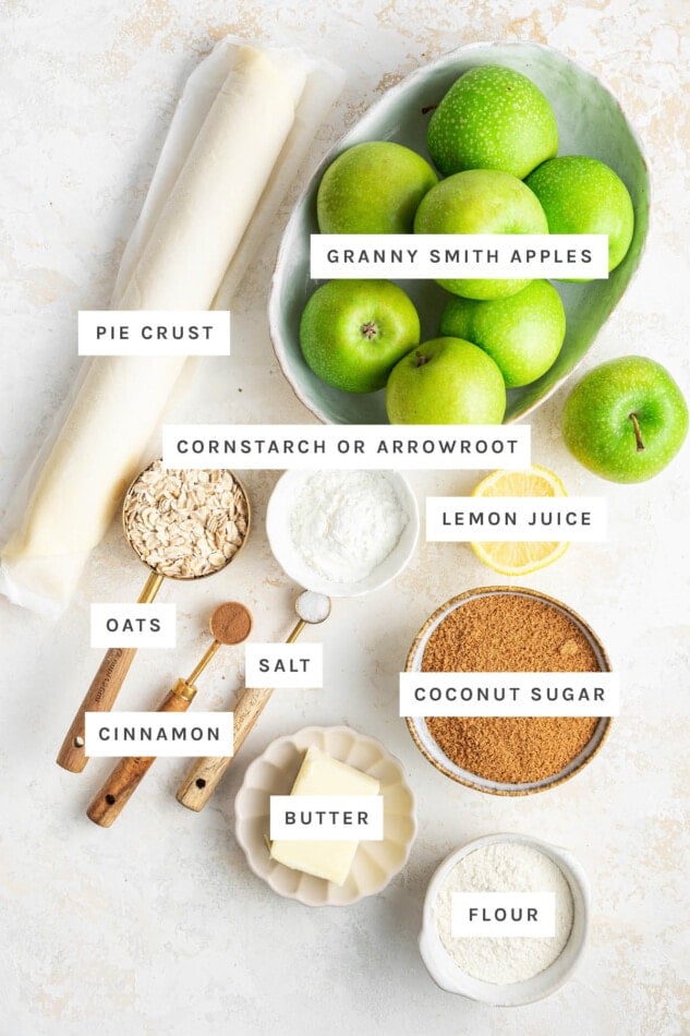 Ingredients measured out to make Healthy Dutch Apple Pie: pie crust, granny smith apples, cornstarch/arrowroot, lemon juice, oats, cinnamon, salt, butter, coconut sugar and flour.