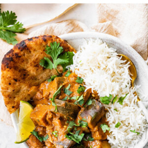 Eggplant curry plated with naan, lime, cilantro and rice.