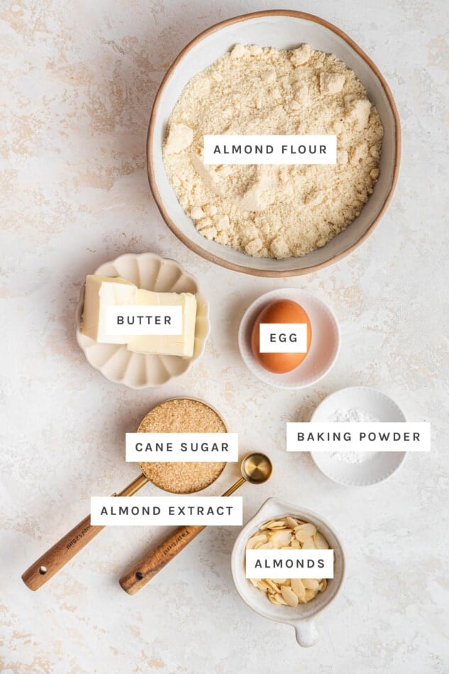 Ingredients measured out to make Almond Cookies: almond flour, butter, egg, cane sugar, baking powder, almond extract and almonds.