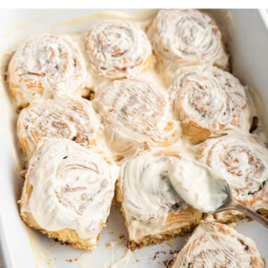 Gluten-free cinnamon rolls in a baking dish topped with a cream cheese frosting.