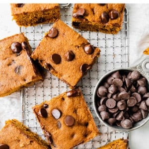 Chocolate chip pumpkin bars on a cooling rack. Cup of chocolate chips is next to the bars.