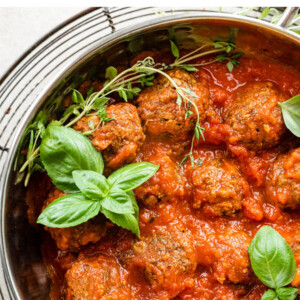 Vegan lentil meatballs, fresh basil and fresh time in a pot with sauce.