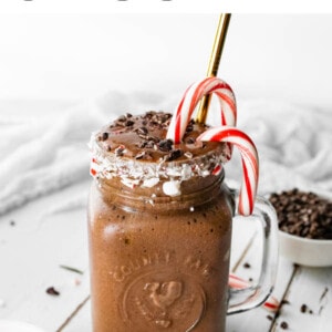 A chocolate peppermint smoothie in a glass mug topped with candy canes, chocolate shavings and a metal straw.