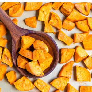 Chunks of roasted sweet potatoes on a baking sheet with a wooden spoon scooping some up.