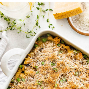 A baking dish containing healthy tuna noodle casserole next to a block of parmesan cheese.