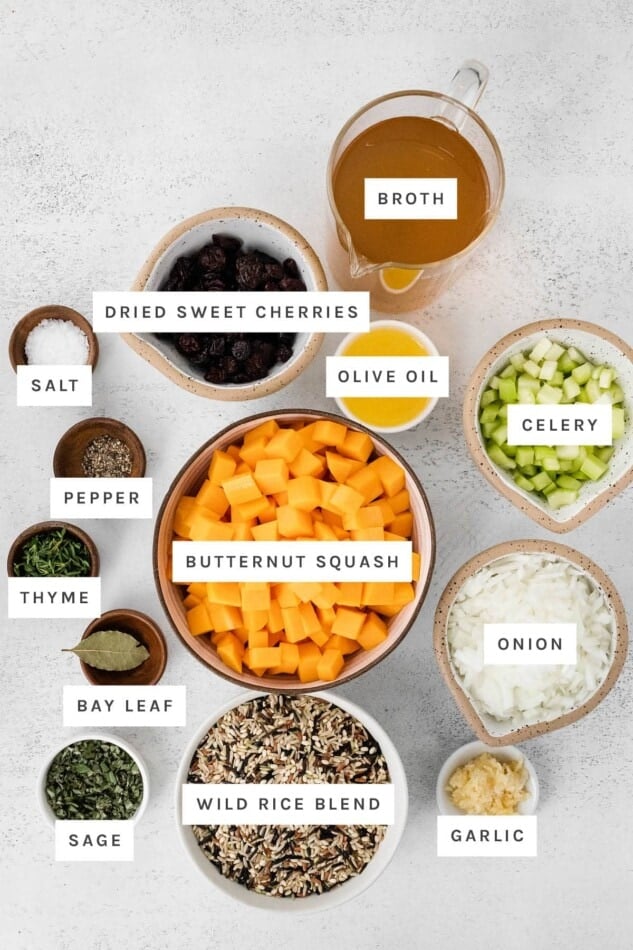 Ingredients measured out to make wild rice stuffing: broth, dried sweet cherries, olive oil, salt, pepper, celery, thyme, butternut squash, bay leaf, onion, sage, wild rice blend and garlic.