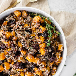 Bowl of wild rice stuffing with butternut squash and dried cherries. Garnished with thyme.