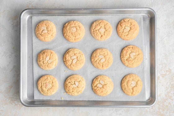 Twelve almond cookies on a baking sheet lined with parchment paper.