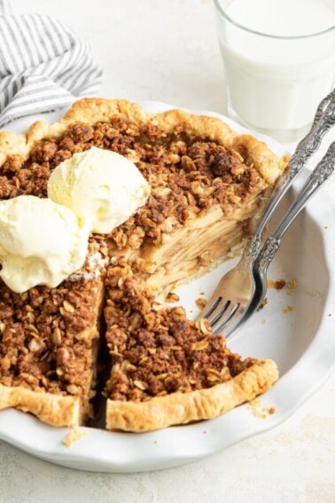 A dutch apple pie topped with ice cream in a pie plate with two forks.