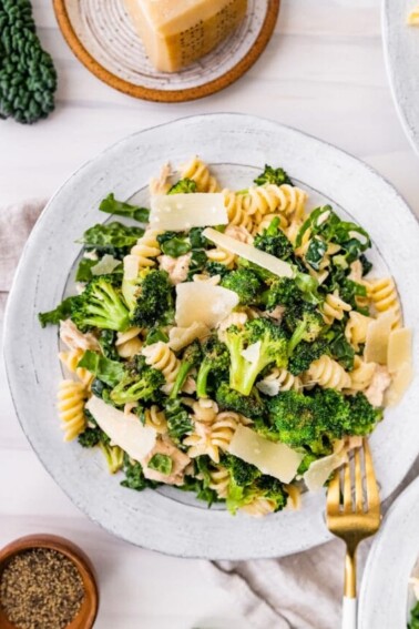 Tuna, broccoli and kale caesar pasta salad on a plate topped with shaved parmesan.