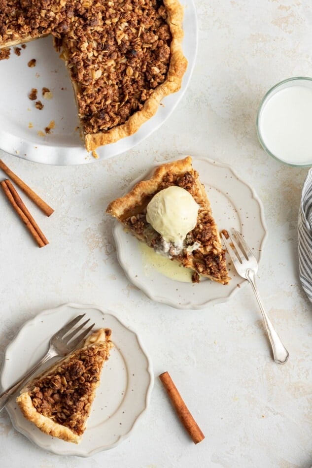 Two slices of dutch apple pie, one topped with vanilla ice cream. The rest of the pie is pictured.
