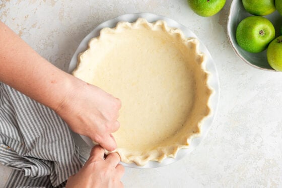 Pie crust fitted to pie plate, being crimped by hand.